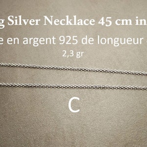 May include: A silver chain necklace, 45 inches long, made of 925 sterling silver. The chain is shown laid out on a brown surface. The text "Sterling Silver Necklace 45 cm in length" and "Cha&icirc;ne en argent 925 de longueur 45 cm" is visible above the chain. The text "2,3 gr" is visible below the chain. The letter "C" is visible below the chain.