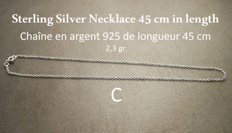 May include: A silver chain necklace, 45 inches long, made of 925 sterling silver. The chain is shown laid out on a brown surface. The text "Sterling Silver Necklace 45 cm in length" and "Cha&icirc;ne en argent 925 de longueur 45 cm" is visible above the chain. The text "2,3 gr" is visible below the chain. The letter "C" is visible below the chain.