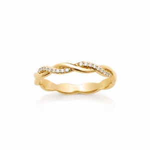 Può includere: Un anello in oro con un design a fascia intrecciata. Una metà della fascia è in oro lucido liscio, mentre l'altra metà è incastonata con una fila di piccole pietre chiare a taglio rotondo che brillano sulla superficie metallica del gioiello.