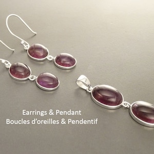 May include: A jewelry set featuring a pair of earrings and a pendant. Each piece has a silver setting and features two oval, deep purple gemstones. The text "Earrings & Pendant" is visible.