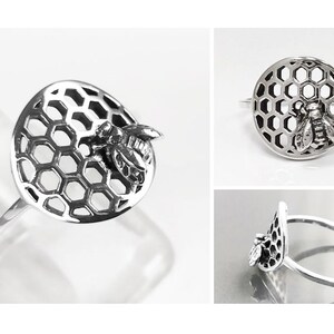 Op de afbeelding: Een zilveren ring met een bij en honingraat ontwerp. De ring is gemaakt van sterling zilver en heeft een gedetailleerd honingraatpatroon met een bij erop.