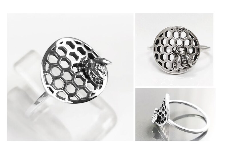 Op de afbeelding: Een zilveren ring met een bij en honingraat ontwerp. De ring is gemaakt van sterling zilver en heeft een gedetailleerd honingraatpatroon met een bij erop.