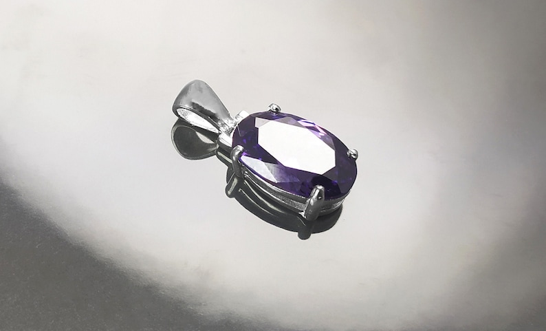 May include: A silver pendant with a large, oval-shaped, purple gemstone.