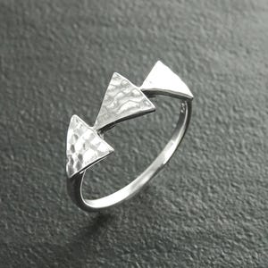 Pode incluir: Um anel de prata com três elementos triangulares dispostos ao longo do topo da banda. Os dois triângulos maiores têm uma superfície martelada texturizada, enquanto o terceiro triângulo menor tem um acabamento liso e polido com brilho.