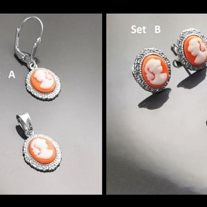 May include: Two sets of jewelry featuring cameo pendants and earrings. Set A includes a pendant and dangle earrings. Set B includes a pendant and stud earrings. All pieces feature a white cameo profile on a peach background.