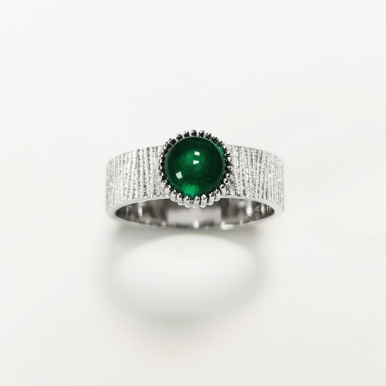 Puede incluir: Un anillo de plata con una banda texturizada y una piedra preciosa verde engastada en un engaste de plata.