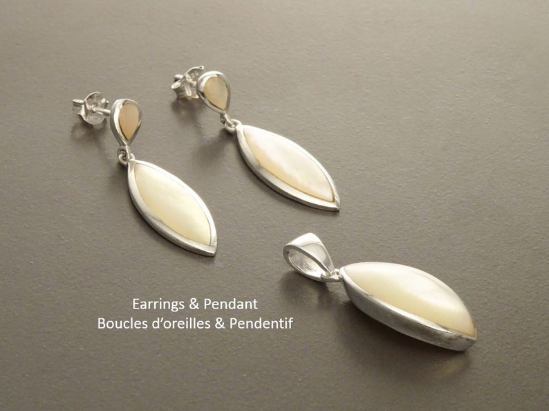 May include: A jewelry set consisting of two drop earrings and one pendant. Each piece features a marquise-shaped white mother-of-pearl inlay set in a polished silver frame. The earrings have a small teardrop accent and post-style backs.