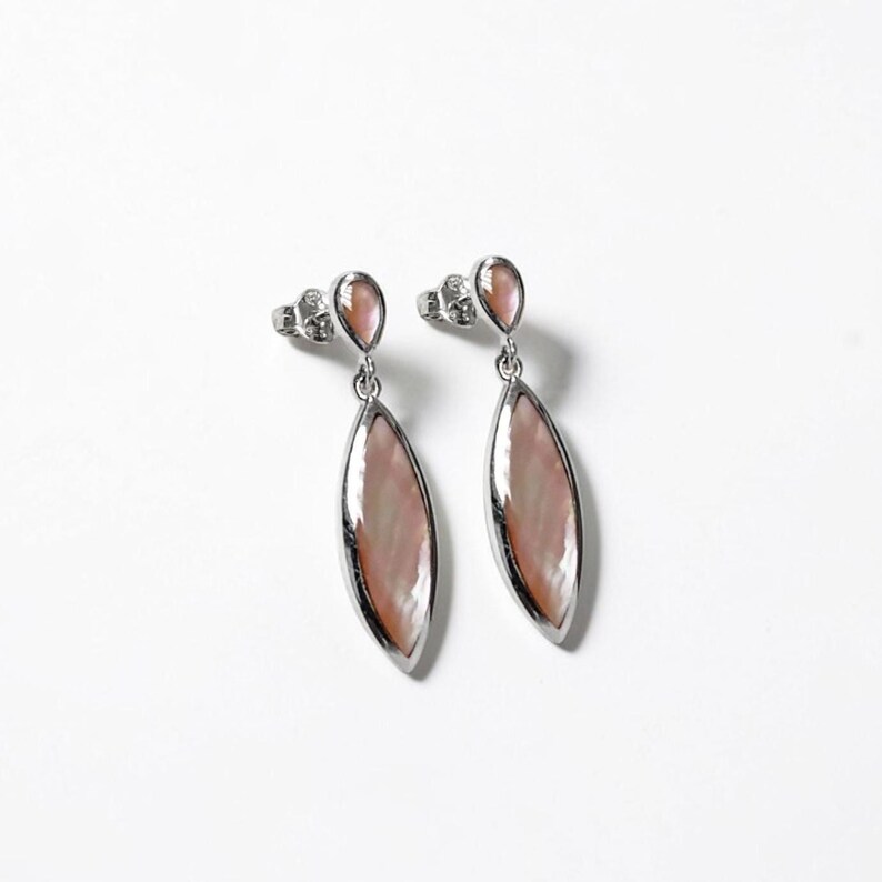 May include: A pair of silver-toned drop earrings featuring a marquise-shaped inlay of iridescent pink mother-of-pearl. Each earring consists of a small circular stud connected to a larger, elongated, pointed oval pendant with a polished metal frame.