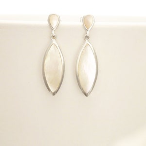May include: A pair of drop earrings featuring a silver-toned metal frame surrounding an elongated, marquise-shaped white mother-of-pearl inlay. Each earring has a small, teardrop-shaped mother-of-pearl accent at the top, connected by a jump ring.