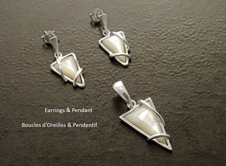 May include: A jewelry set consisting of two triangular earrings and one matching pendant, each featuring a smooth, cream-colored inlay framed in polished silver metal. The text "Earrings & Pendant" and "Boucles d'Oreilles & Pendentif" is visible.