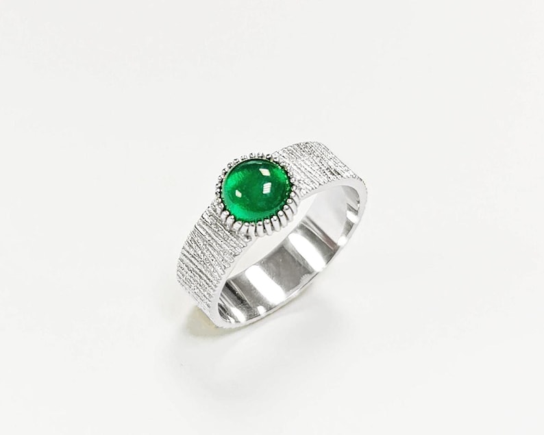 Puede incluir: Un anillo de plata con una banda texturizada y una piedra preciosa verde engastada en un engaste de plata.