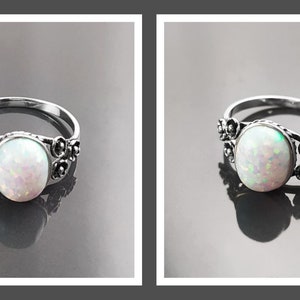 Puede incluir: Un anillo de plata con una piedra de &oacute;palo ovalada e iridiscente. El anillo presenta un dise&ntilde;o floral a cada lado del &oacute;palo. El &oacute;palo es de color blanco nacarado con toques rosados y verdes. El anillo se muestra sobre una superficie reflectante.