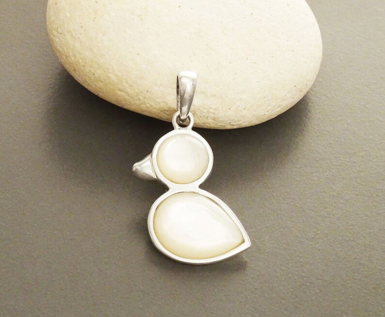 Puede incluir: Un colgante de plata con forma de pato con dos piedras blancas de n&aacute;car.