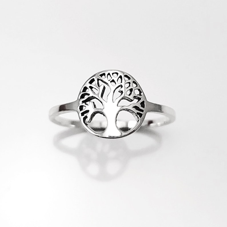 May include: A silver ring featuring a tree of life design. The ring is circular and the tree is cut out of the metal.