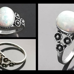 Puede incluir: Anillo de plata con una piedra de &oacute;palo ovalada e iridiscente. El anillo tiene un dise&ntilde;o floral en la banda. El &oacute;palo muestra un juego de colores con destellos blancos y otros tonos. Joya.