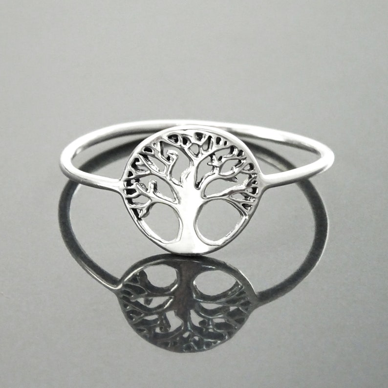 May include: A silver ring featuring a tree of life design. The ring is thin and delicate, and the tree is detailed and intricate.