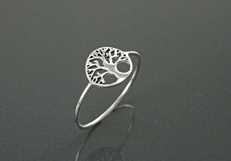 May include: A silver ring featuring a tree of life design. The ring has a thin band and a circular tree of life pendant.