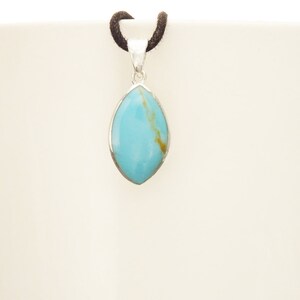 Puede incluir: Un colgante de plata con una piedra turquesa azul claro en forma de marquesa. El colgante est&aacute; colgado de un cord&oacute;n negro.