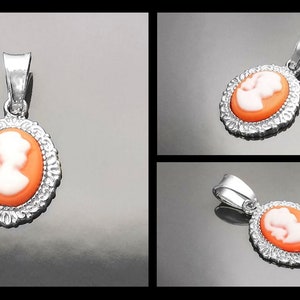 May include: A silver pendant with a cameo featuring a white profile of a person on an orange background. The cameo is surrounded by a silver filigree design.
