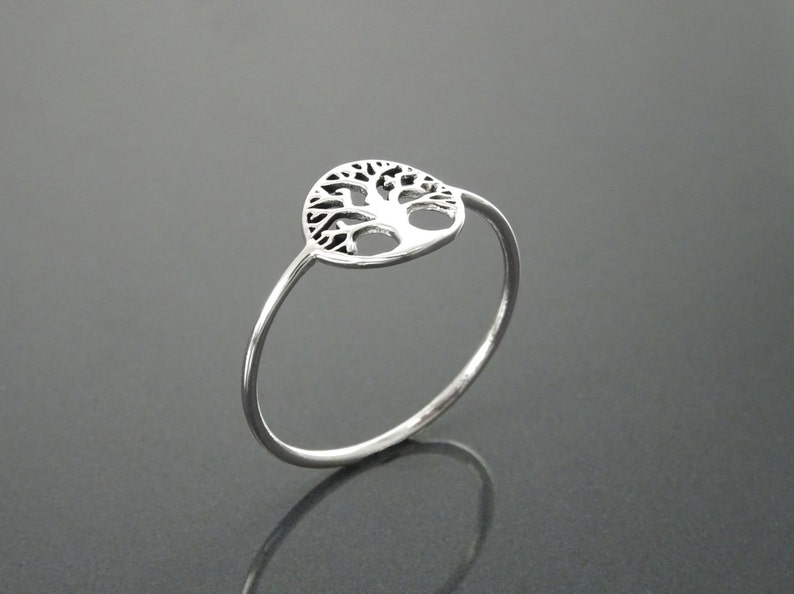 May include: A silver ring featuring a tree of life design. The ring is simple and delicate, with a thin band and a circular tree of life design.