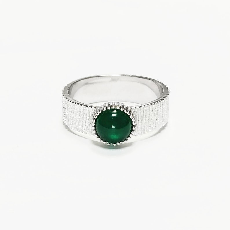 Puede incluir: Un anillo de plata con una banda texturizada y una piedra preciosa verde engastada en un engaste de plata.