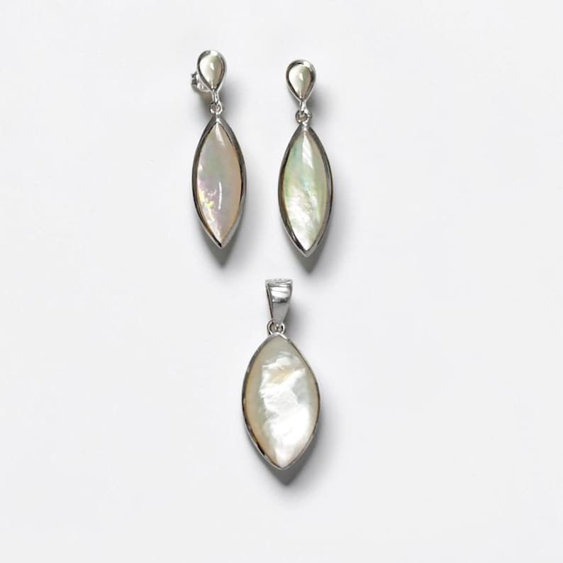 May include: A jewelry set consisting of two marquise-shaped drop earrings and a matching pendant. Each piece features a smooth, iridescent mother-of-pearl inlay set within a polished silver-toned metal frame, showcasing a subtle pearlescent sheen.