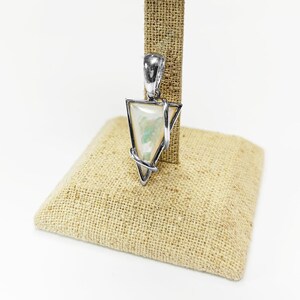 May include: A triangular pendant featuring a smooth, iridescent white stone with subtle green and blue flashes, encased in a polished silver-toned metal frame that wraps around the edges and includes a sturdy bail at the top for hanging.