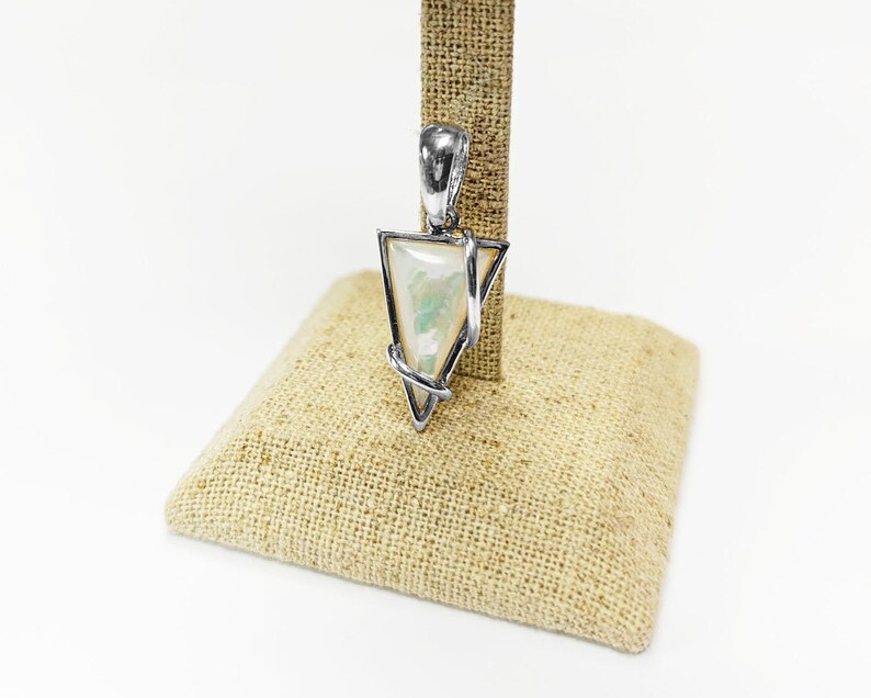May include: A triangular pendant featuring a smooth, iridescent white stone with subtle green and blue flashes, encased in a polished silver-toned metal frame that wraps around the edges and includes a sturdy bail at the top for hanging.