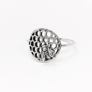 Op de afbeelding: Een zilveren ring met een bij- en honingraatontwerp. De ring is gemaakt van sterling zilver en heeft een gedetailleerd bijontwerp.