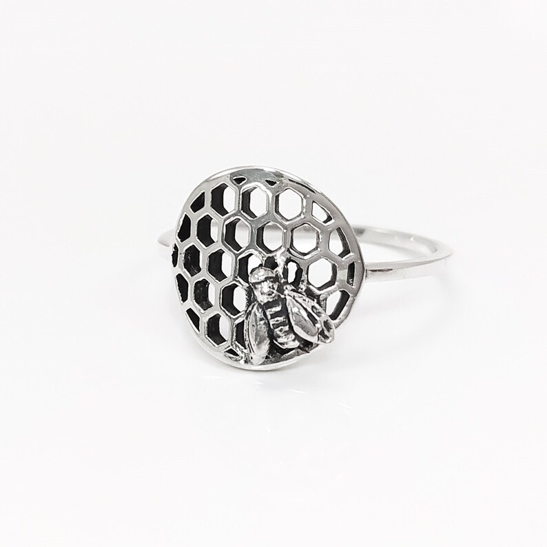 Op de afbeelding: Een zilveren ring met een bij- en honingraatontwerp. De ring is gemaakt van sterling zilver en heeft een gedetailleerd bijontwerp.