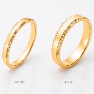 Pode incluir: Dois anéis dourados com faixas texturizadas em fundo branco. Um anel é rotulado 3 mm (M), o outro 4 mm (L). Anéis de casamento ou noivado.