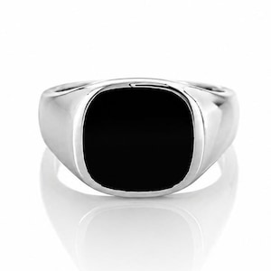Op de afbeelding: Een gepolijste zilveren ring met een vierkante, zwarte onyx steen. De ring heeft een reflecterend oppervlak en staat tegen een witte achtergrond. De zegelring is een klassiek ontwerp.