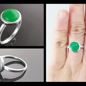 May include: A silver ring featuring a round, bright green gemstone. The gemstone is set in a bezel setting, and the ring has a simple, elegant band. The ring is shown in multiple views, including a close-up and on a finger.