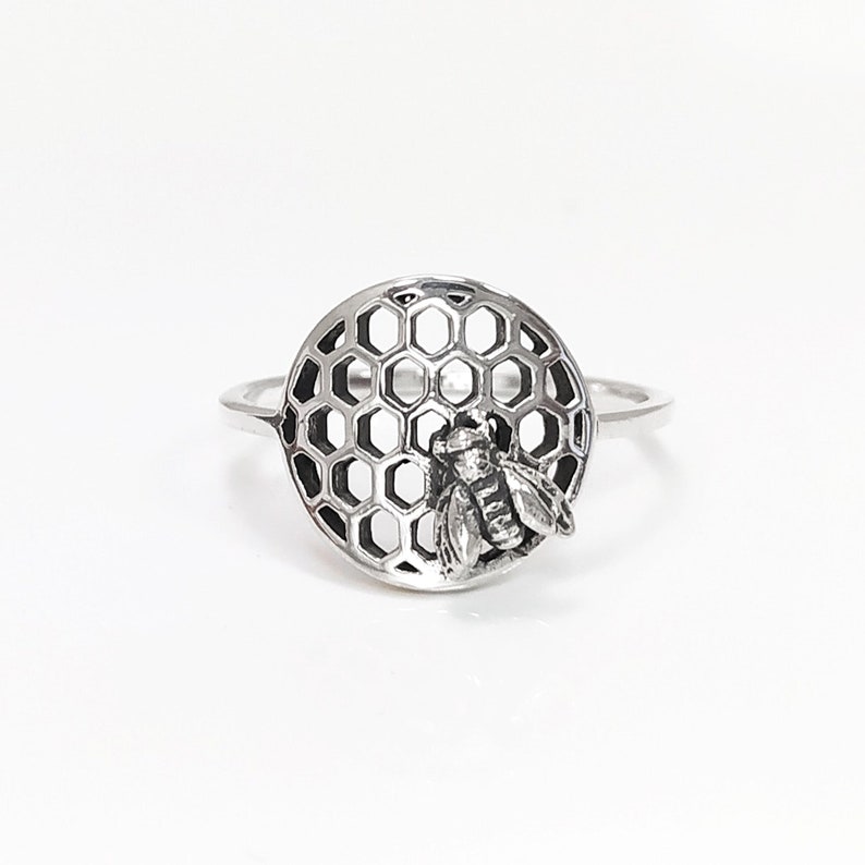 Op de afbeelding: Zilveren ring met een bij op een honingraatontwerp. De ring is een delicaat sieraad met een gedetailleerd ontwerp.