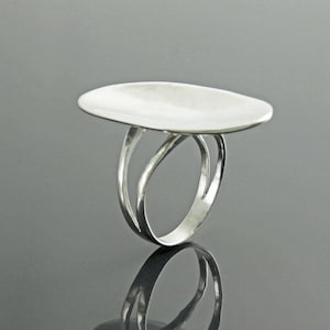 K&ouml;nnte beinhalten: Ein silberner Ring mit einer breiten, flachen, ovalen Oberseite. Der Ringband ist doppelt gefasst und hat ein gedrehtes Design.