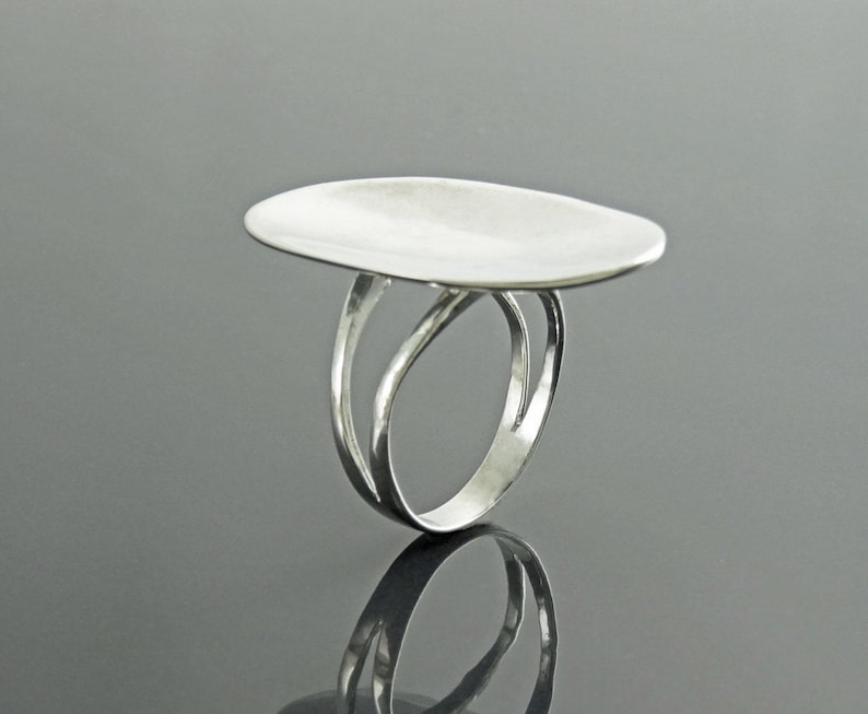 K&ouml;nnte beinhalten: Ein silberner Ring mit einer breiten, flachen, ovalen Oberseite. Der Ringband ist doppelt gefasst und hat ein gedrehtes Design.
