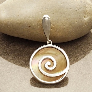 Può includere: Un ciondolo d'argento con un'incisione rotonda in madreperla iridescente con un motivo a spirale d'argento.