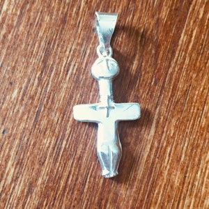 May include: A silver pendant in the shape of a cross with a human figure on it.