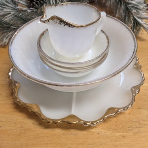 May include: A set of white milk glass dishes with gold trim. The set includes a creamer, two bowls, a larger bowl, and a scalloped serving plate.