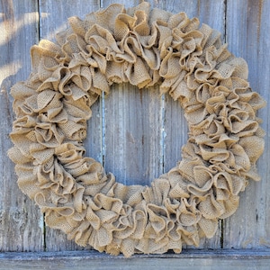 May include: A brown burlap wreath with a ruffled texture. The wreath is made of burlap fabric and is a popular choice for rustic home decor.