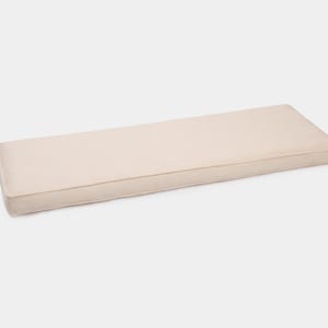 May include: A rectangular bench cushion in a solid light beige color. The cushion features a smooth, flat top surface with defined, stitched edges that create a clean, structured profile. The fabric has a uniform, matte texture throughout.