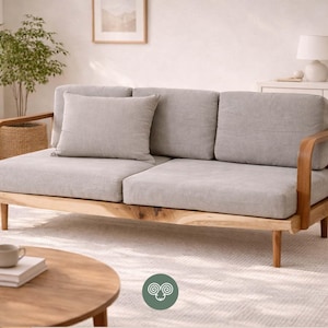 May include: A three-seat sofa featuring light gray fabric upholstery, a matching throw pillow, and a natural wood frame with curved armrests and tapered legs. The sofa has a low-profile design with three back cushions and two seat cushions.