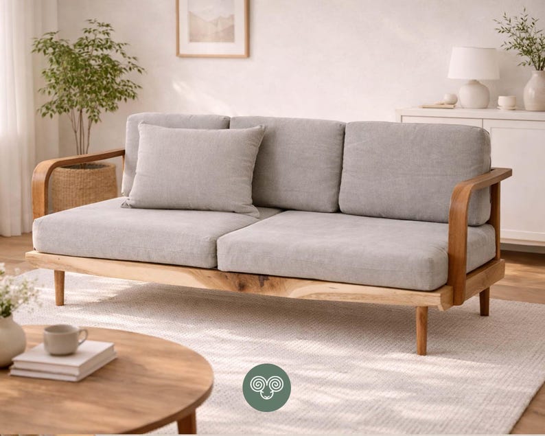 May include: A three-seat sofa featuring light gray fabric upholstery, a matching throw pillow, and a natural wood frame with curved armrests and tapered legs. The sofa has a low-profile design with three back cushions and two seat cushions.