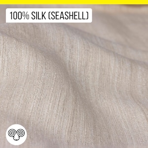 Peut inclure: Gros plan sur un tissu doux de couleur blanc cassé avec une texture subtile. Le tissu est étiqueté "100% SOIE (COQUILLAGE)" et porte un symbole de laine.