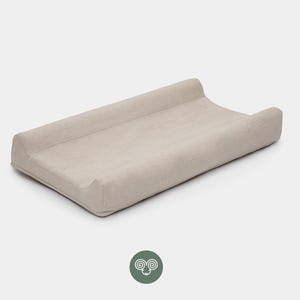 Könnte beinhalten: Eine rechteckige Wickelauflage mit einem hellbeigen Stoffbezug. Die Auflage verfügt über erhöhte, konturierte Seitenränder und eine flache, glatte Mitteloberfläche. Das Design ist schlicht und funktional und bietet eine neutrale Unterlage.