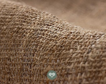 May include: A close-up view of a coarse, brown, woven fabric with a visible grid-like texture. The material features thick, natural-colored fibers interlaced in a simple over-under pattern, creating a rough, tactile surface with small gaps.