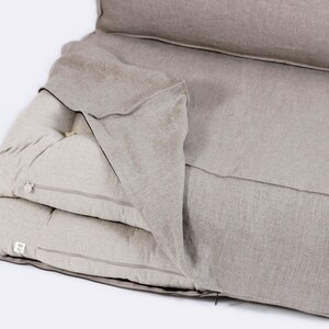 May include: A beige linen futon mattress with a zippered cover. The mattress is folded in half and the cover is pulled back to reveal the layers of the mattress.