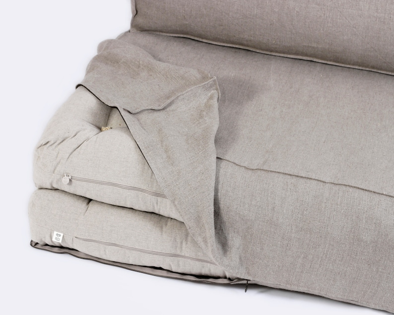 May include: A beige linen futon mattress with a zippered cover. The mattress is folded in half and the cover is pulled back to reveal the layers of the mattress.
