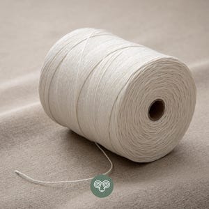 May include: A large spool of off-white cotton yarn or twine wound into a cylindrical shape. The spool features a central cardboard core and a single loose strand extending from the bottom, showcasing a smooth, tightly wound texture throughout.