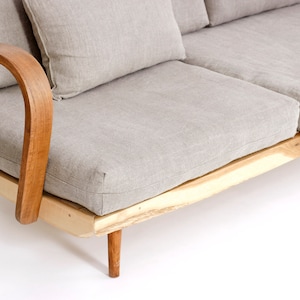 May include: A sofa featuring a light beige fabric upholstery with matching cushions, supported by a natural light-colored wooden frame with curved armrests and tapered legs. The base of the frame displays a raw, live-edge wood texture.